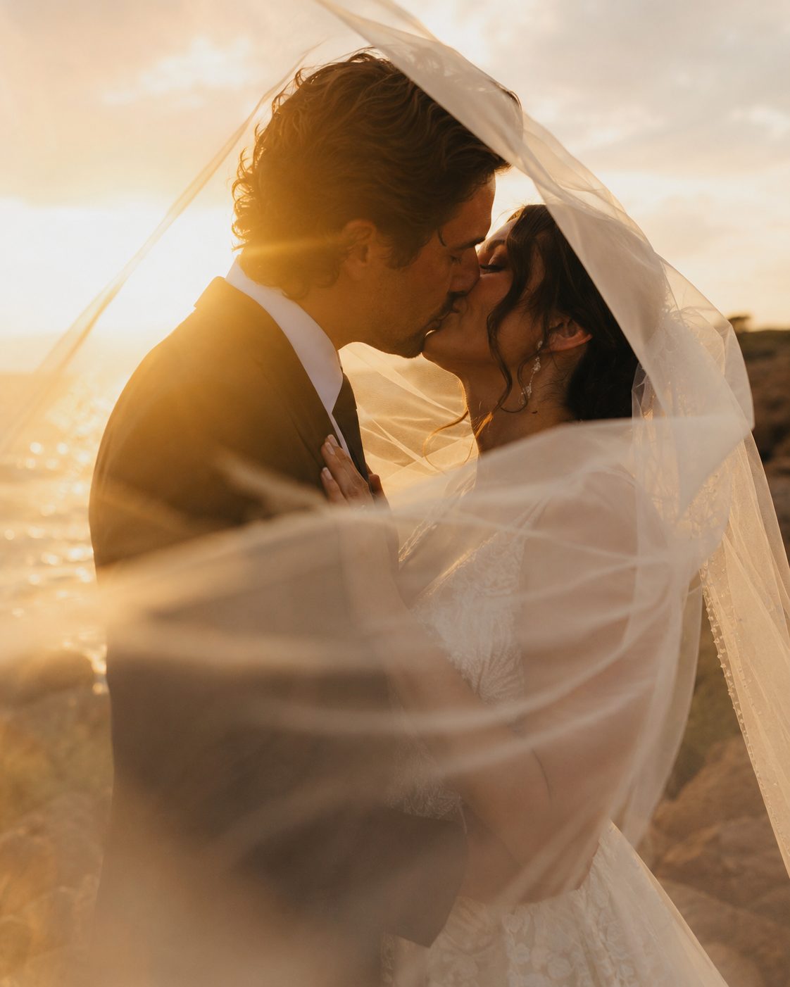 A couple kissing under a wedding veil at sunset